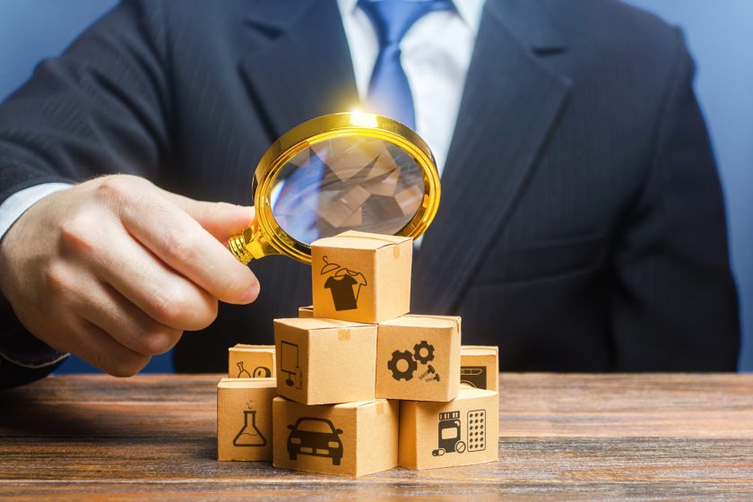 A businessman examines boxes goods with magnifying glass. Market structure research, find unoccupied target consumer niches, demand assessment. Marketing sales promotion strategy. Retailer